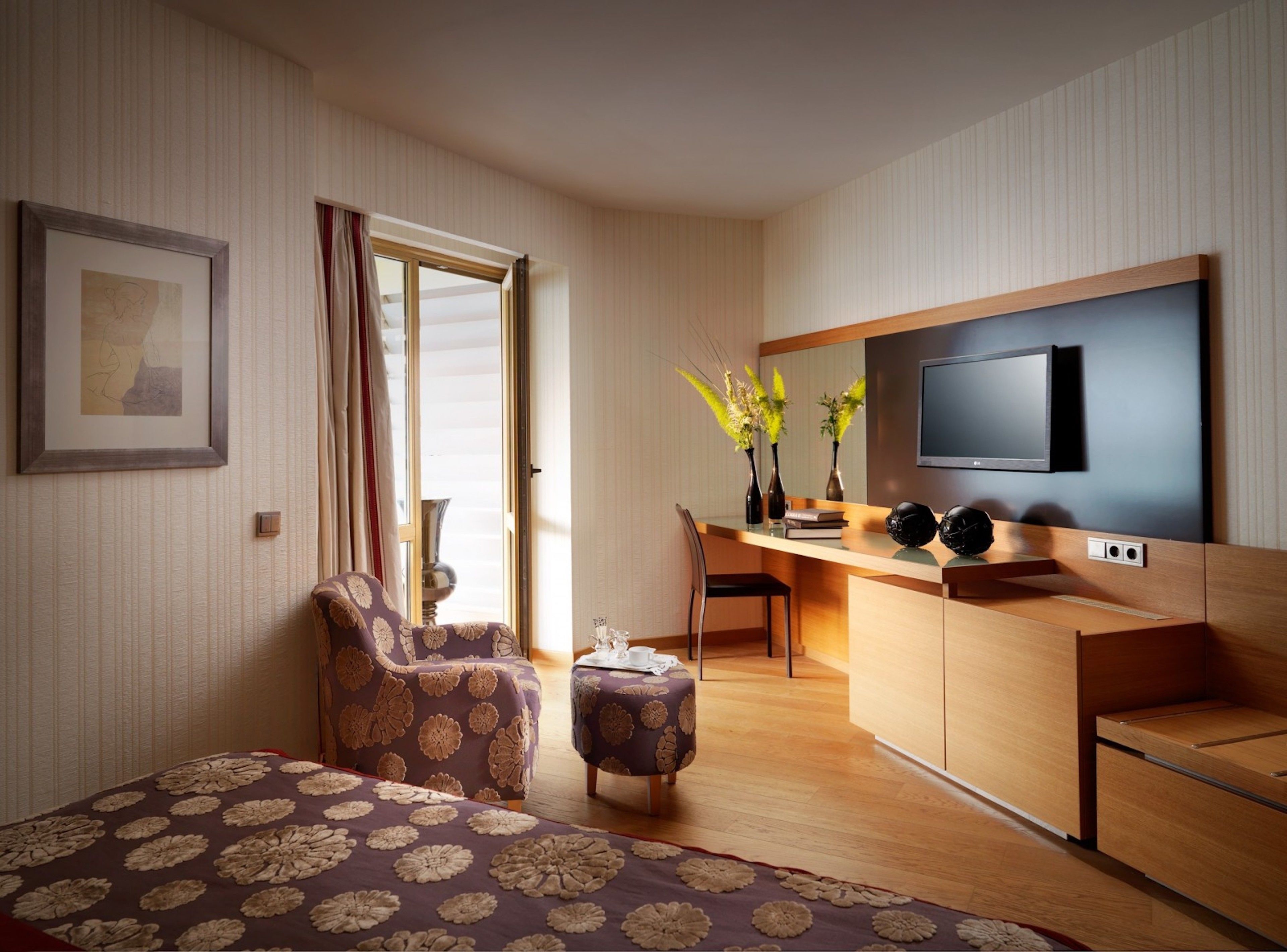 A modern hotel room with a bed, a desk, a chair, a TV, and a window with curtains.