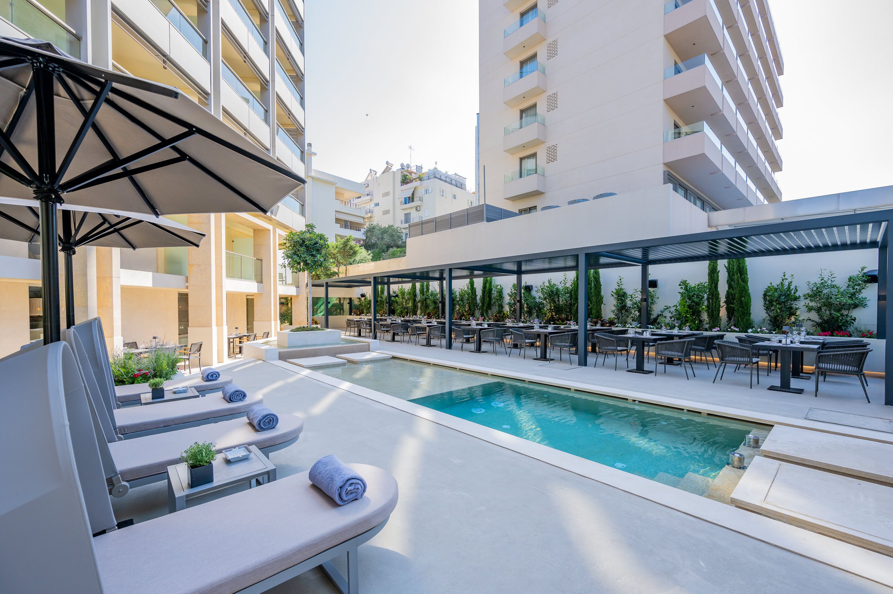 A rooftop pool area with lounge chairs, umbrellas, and outdoor dining tables.