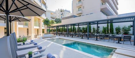 A rooftop pool area with lounge chairs, umbrellas, and outdoor dining tables.