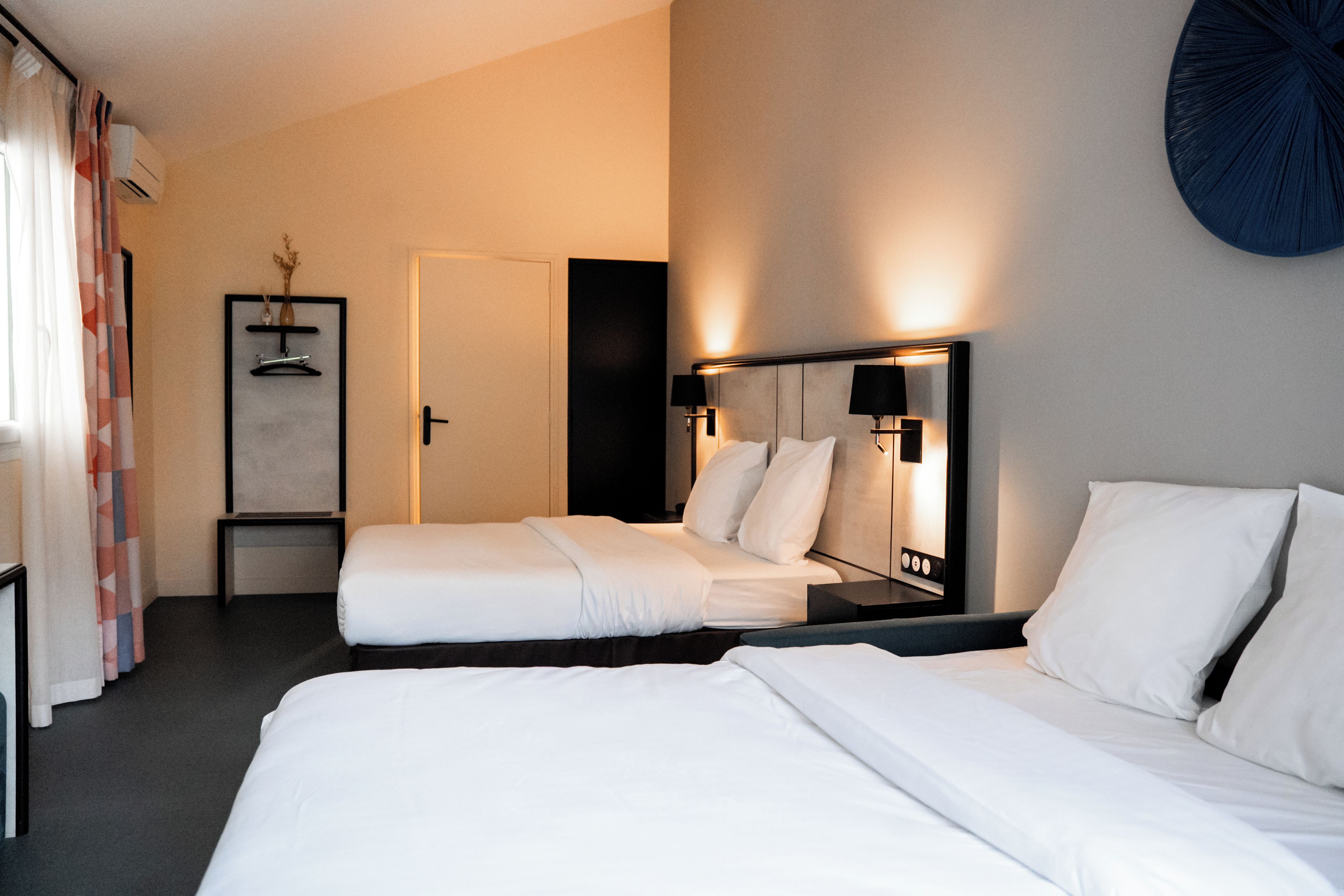 Habitación de hotel con dos camas, una mesita de noche, un espejo y una lámpara de pared.