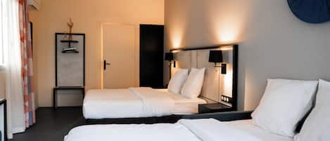 A hotel room with two beds, a bedside table, a mirror, and a wall-mounted lamp.