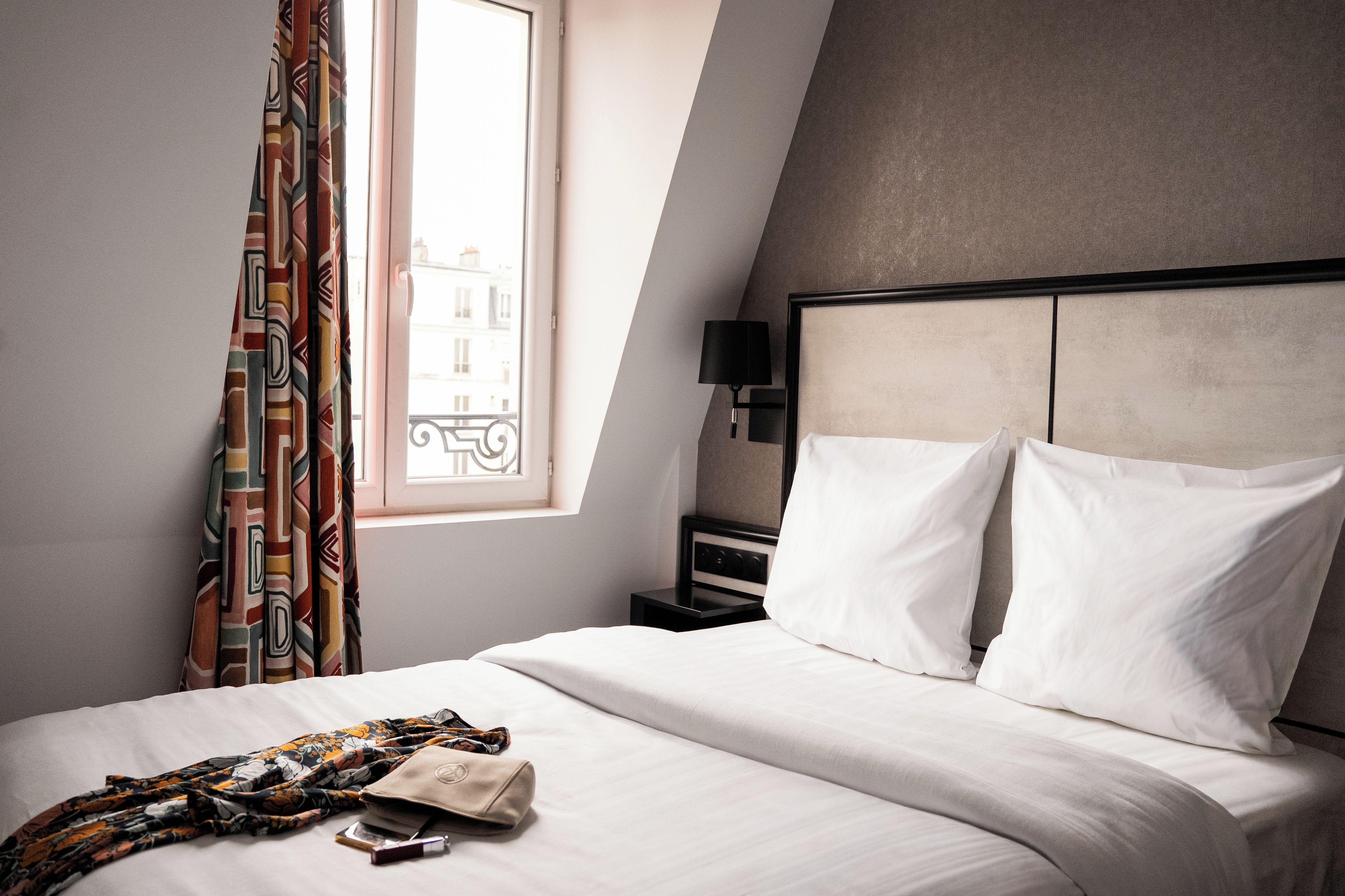 Ein Hotelzimmer mit Bett, Nachttisch, Lampe und einem Fenster mit Vorhängen.