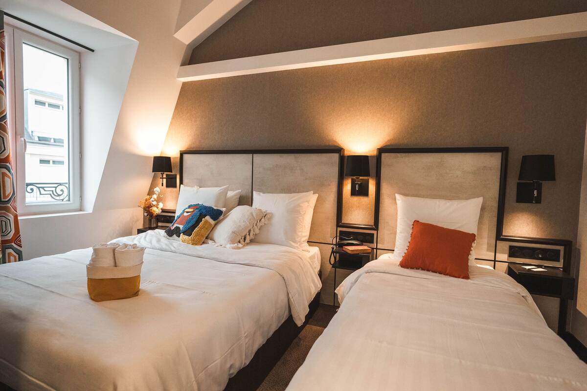 A hotel room with two beds, a window with a view, and bedside lamps.