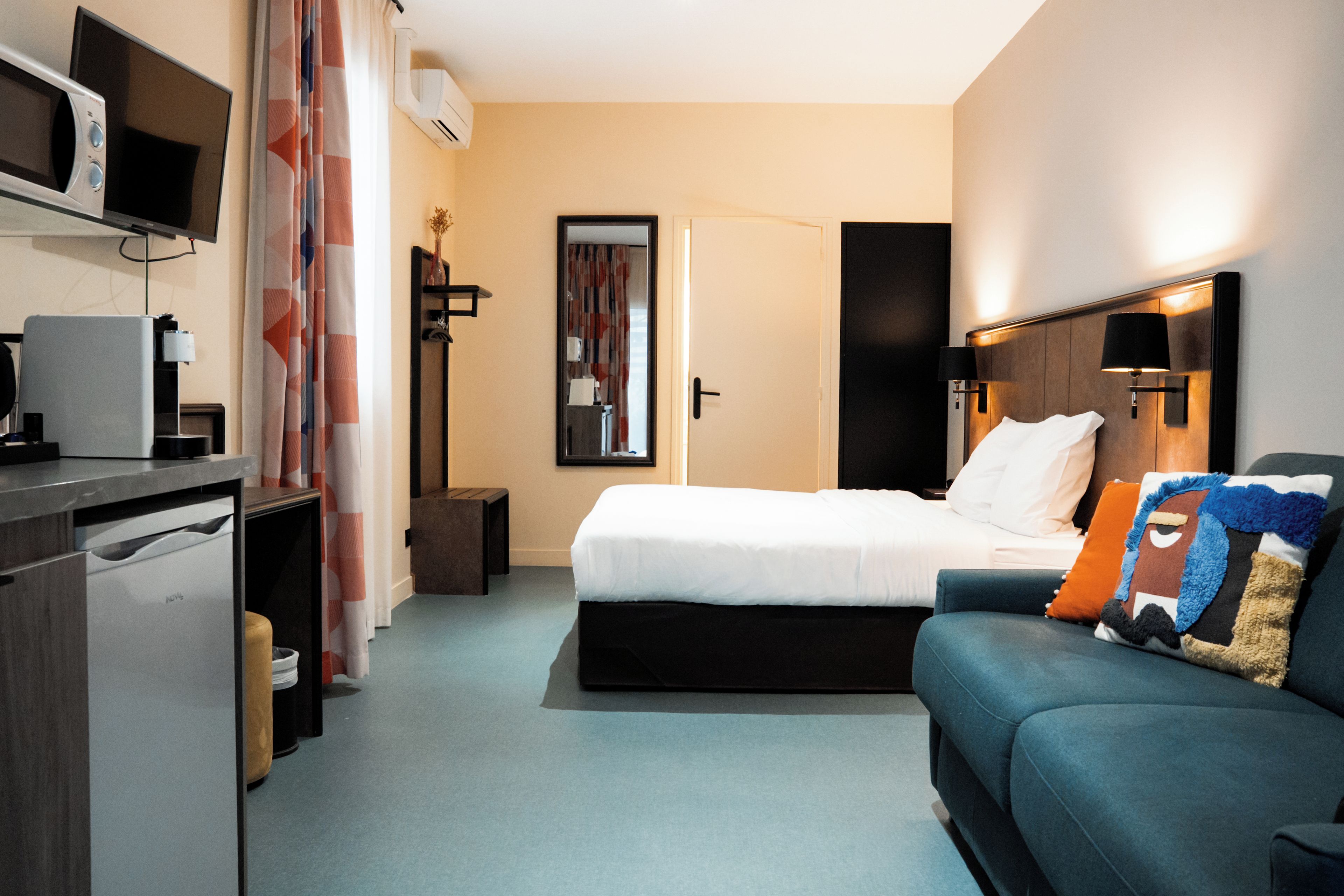 A hotel room with a bed, a desk with a computer, a TV, and a sofa.