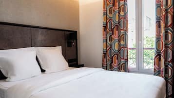 Quarto de hotel com cama, mesa de cabeceira, abajur e janela com cortinas.