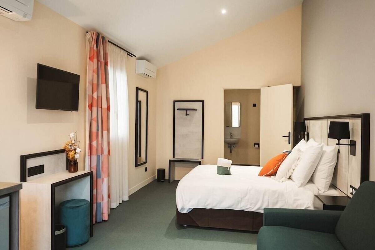 A hotel room with a bed, a desk, a chair, a TV, a mirror, and a bathroom.