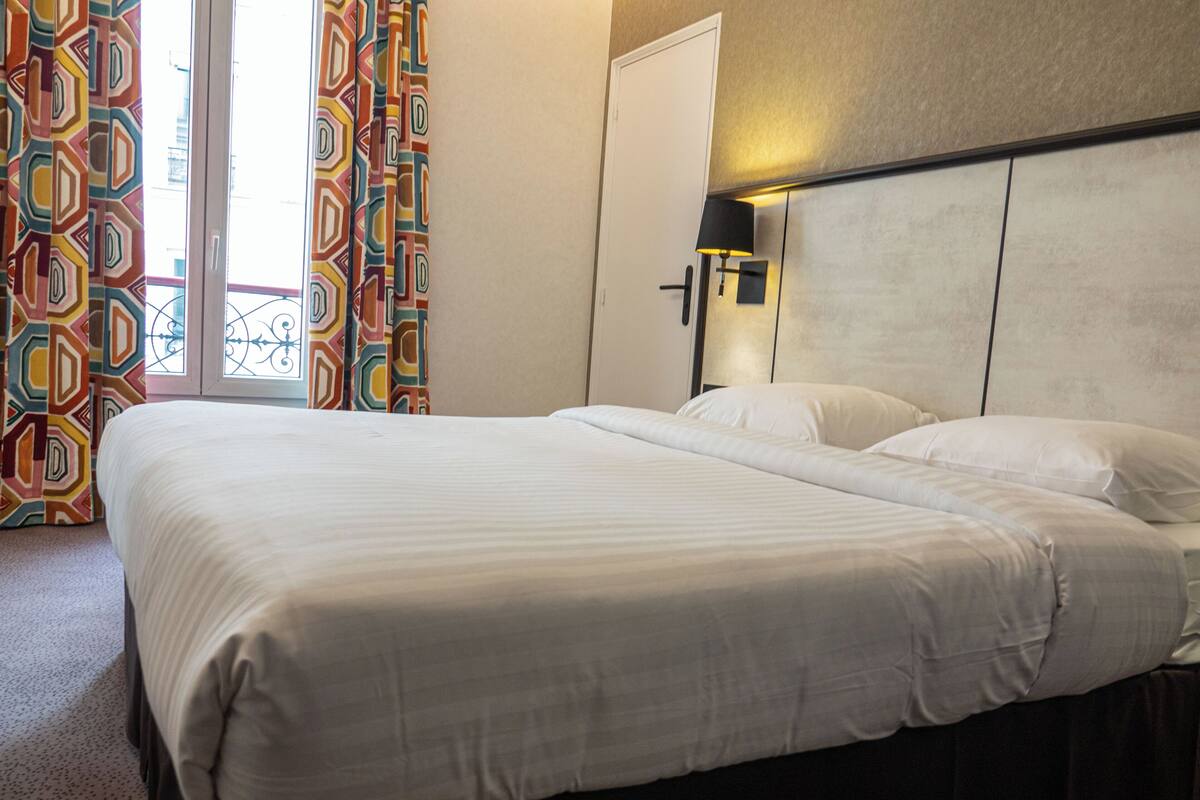 A hotel room with a large bed, a nightstand with a lamp, and a door with a handle.
