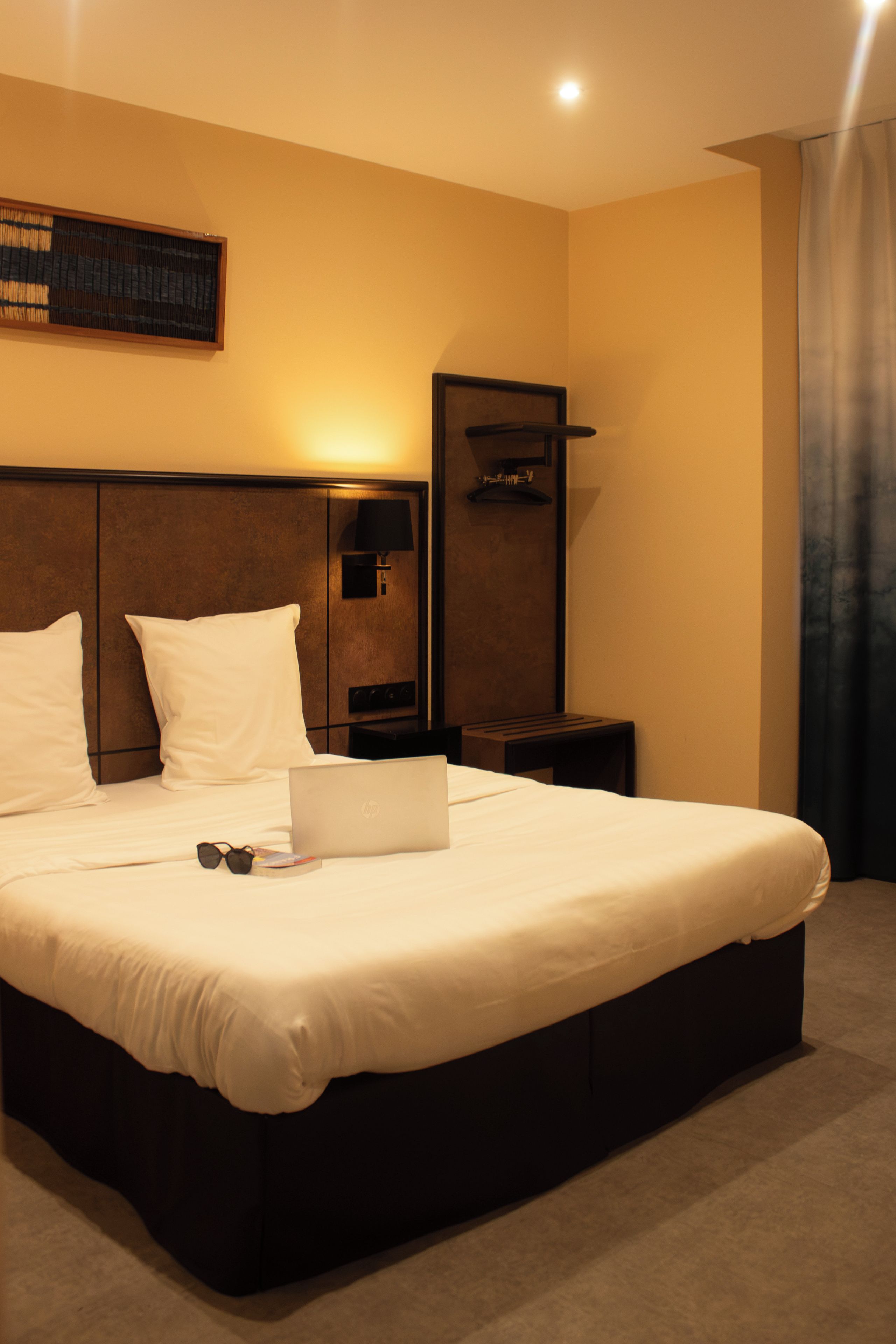 A hotel room with a large bed, a bedside table, a lamp, and a laptop.