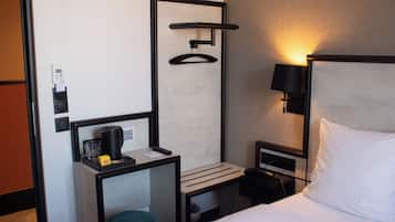 Une chambre d’hôtel comprenant un lit, une table de chevet avec une lampe, une petite table avec une machine à café et un téléphone fixé au mur.