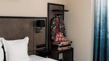 Een hotelkamer met een bed, een nachtkastje, een koffer, een kapstok en een wandlamp.