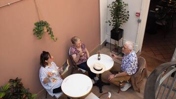 A group of people seated around a table in an outdoor setting with potted plants and a tiled floor.