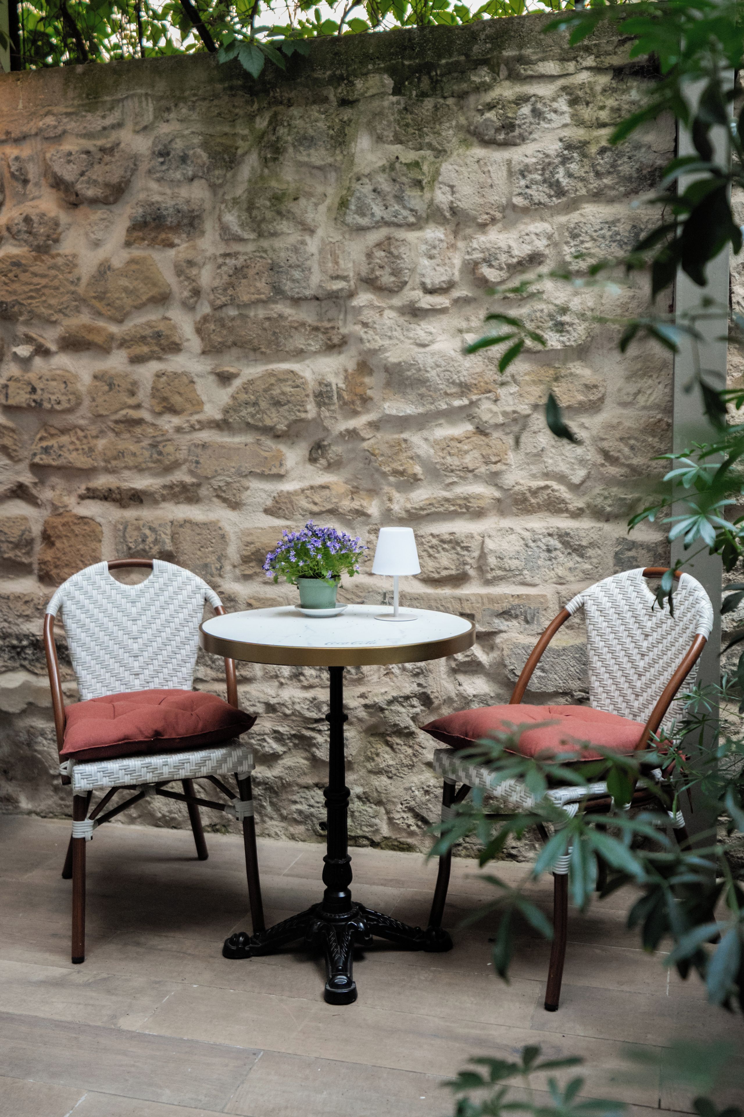 Un muro de piedra con dos sillones de mimbre y una mesa redonda con una lámpara y una planta en maceta.