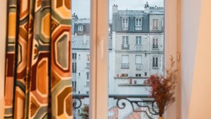 Una ventana con vistas a edificios, una cortina y un florero con plantas secas.
