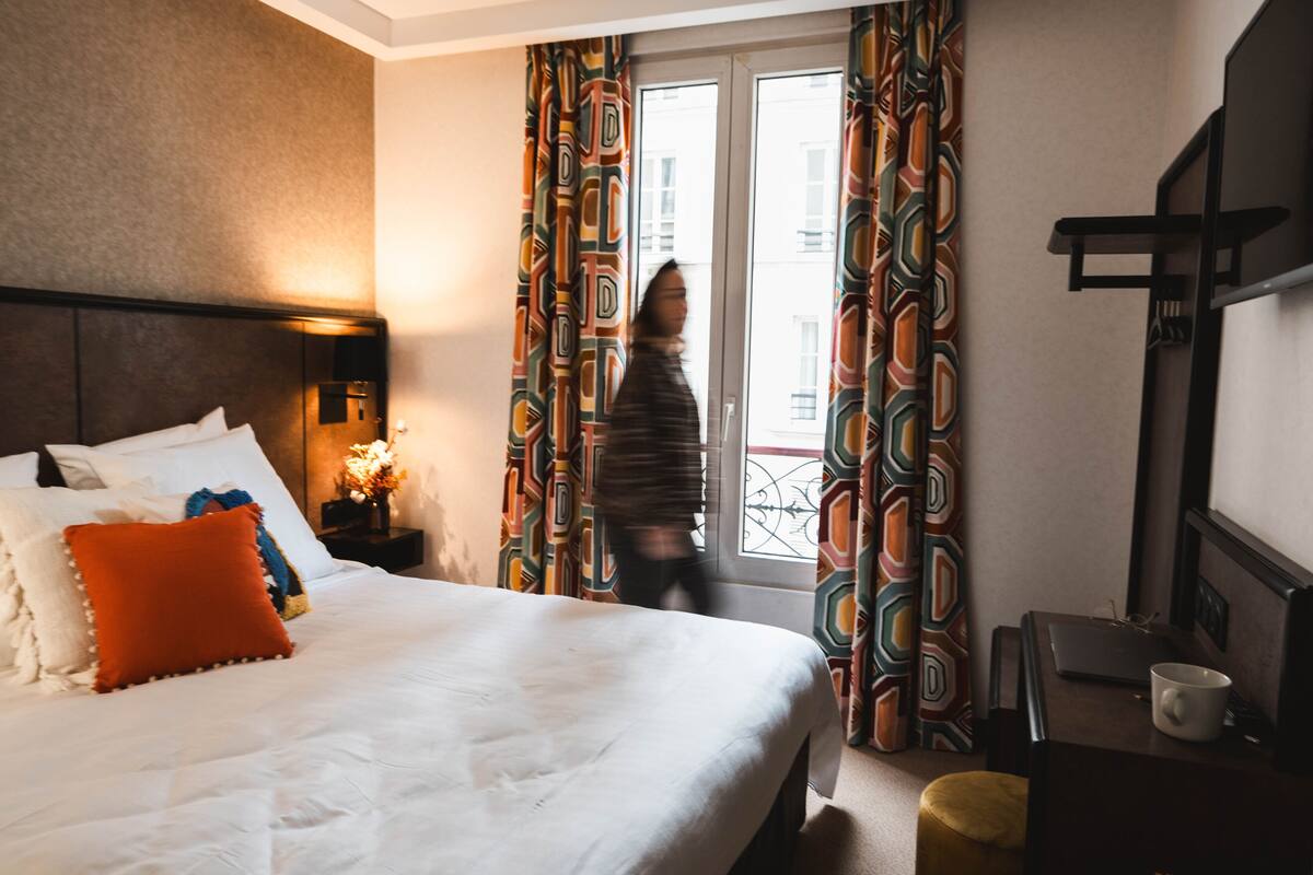 A hotel room with a large bed, a bedside table with a lamp, and curtains with a geometric pattern.