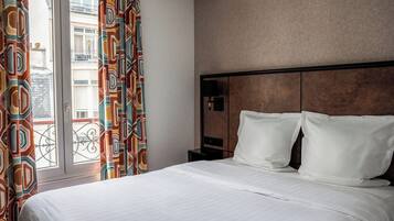 A hotel room with a bed, a nightstand, a lamp, and a view of the outside.