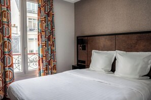A hotel room with a bed, a nightstand, a lamp, and a view of the outside. - Hotel La Maison Montparnasse (Paris)