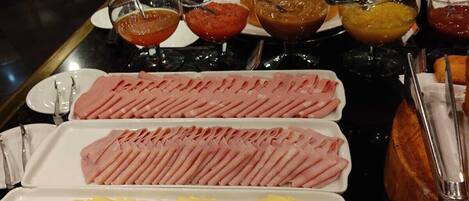Un bufé con diversos alimentos, incluyendo carnes, quesos y postres.