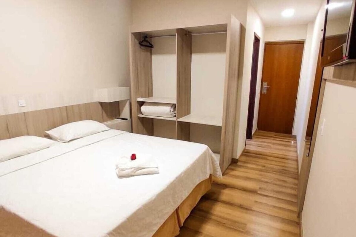 Una habitación de hotel con una cama, suelo de madera, un armario y una puerta.