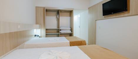 Habitación de hotel con dos camas, un televisor montado en la pared, un armario y una mesita de noche con lámpara.