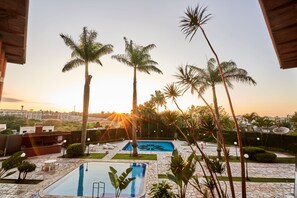A swimming pool with a view of the sunset, surrounded by palm trees and a stone patio.