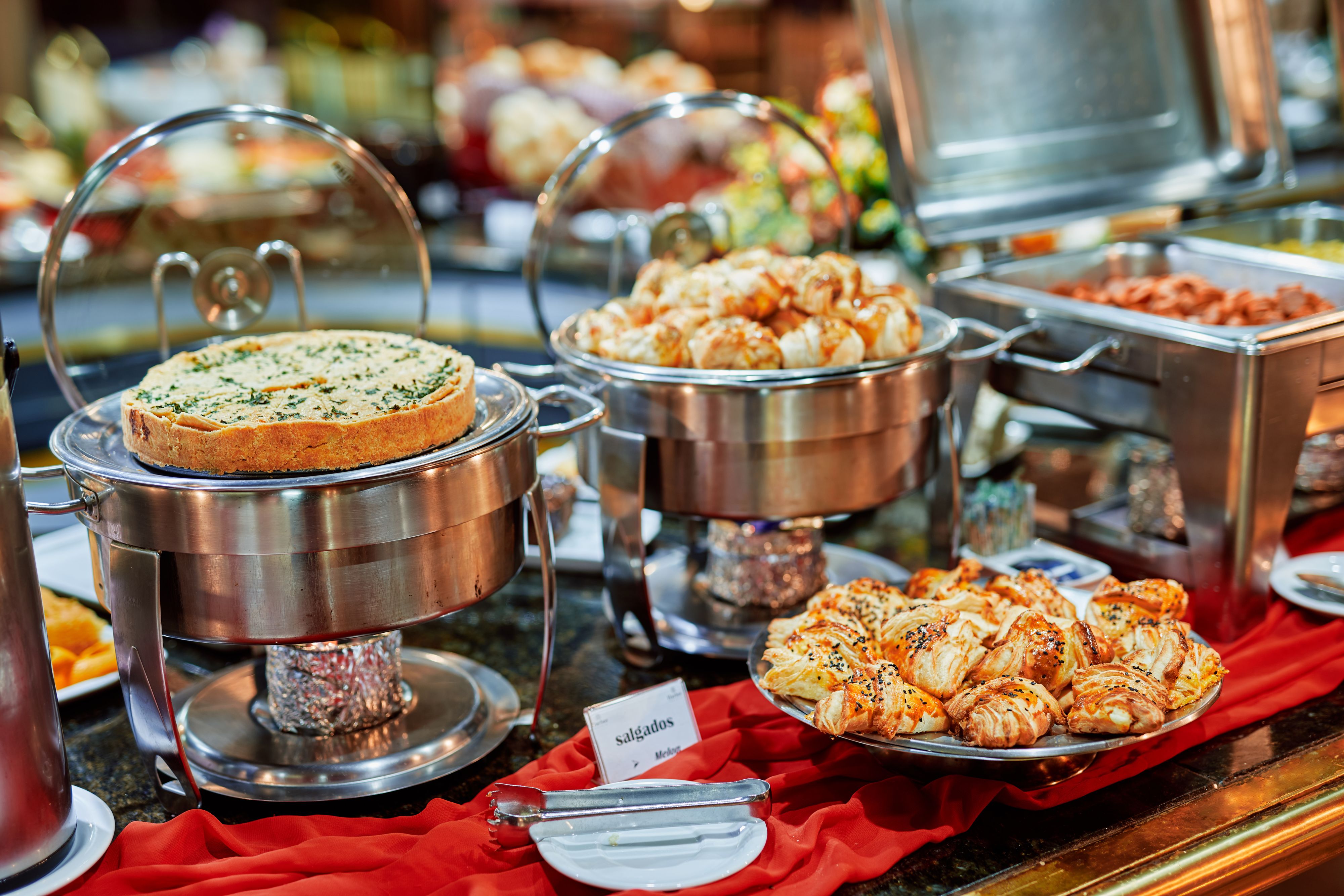 A buffet with various food items, including a covered dish, a tray of pastries, and a container of meat.