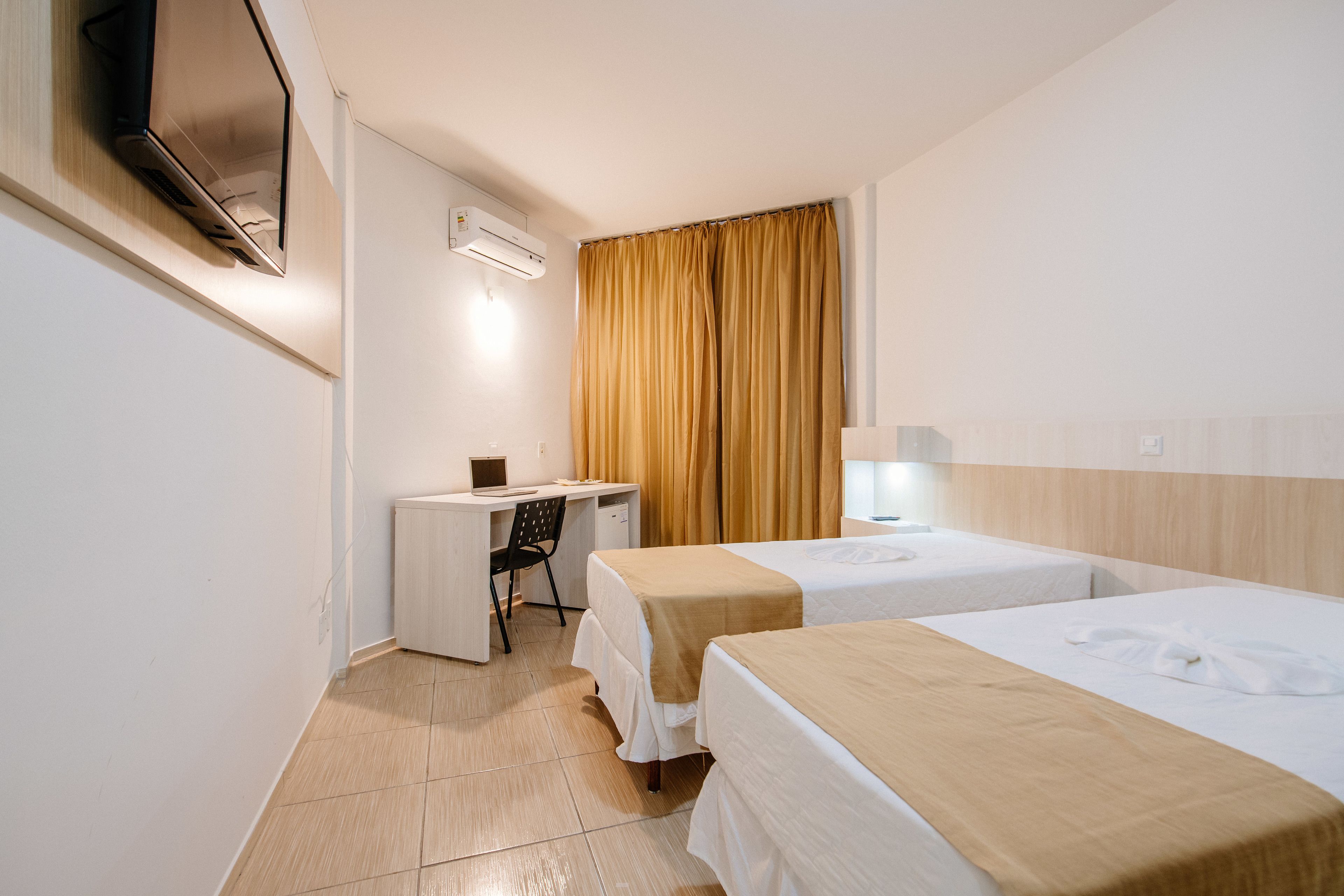 A hotel room with two beds, a desk, a chair, and a TV.