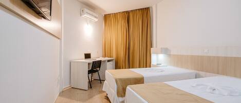 A hotel room with two beds, a desk, a chair, and a TV.