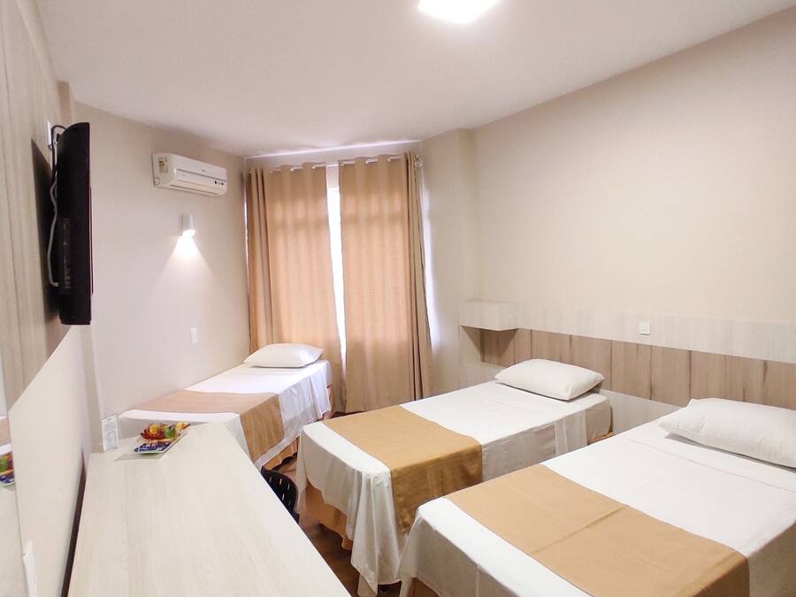A hotel room with two single beds, a desk with a chair, a flat-screen TV, and an air conditioning unit.