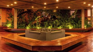 A modern indoor space with a central water feature surrounded by lush greenery and wooden flooring.