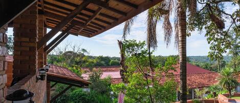 A covered patio with a brick wall, hanging lanterns, and a view of a lush garden and distant buildings.