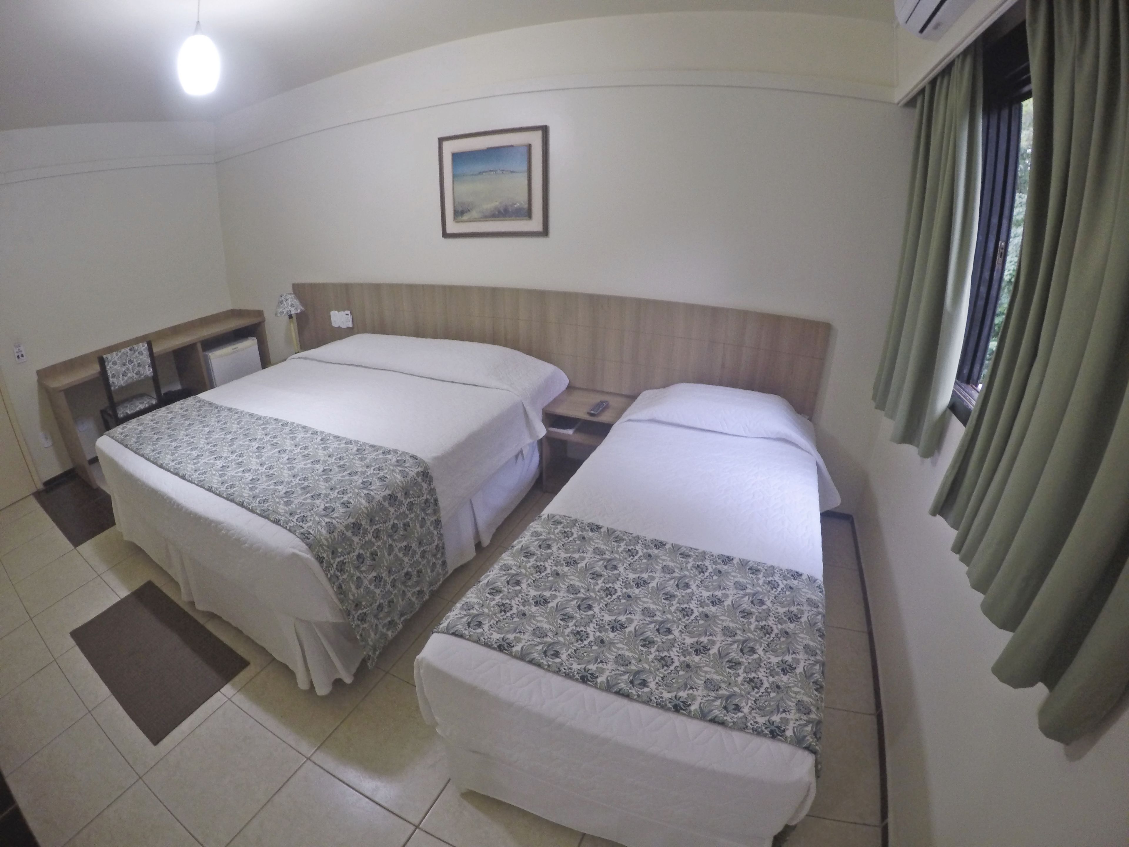 A hotel room with two beds, a desk, a chair, a nightstand, a picture on the wall, and a window with curtains.