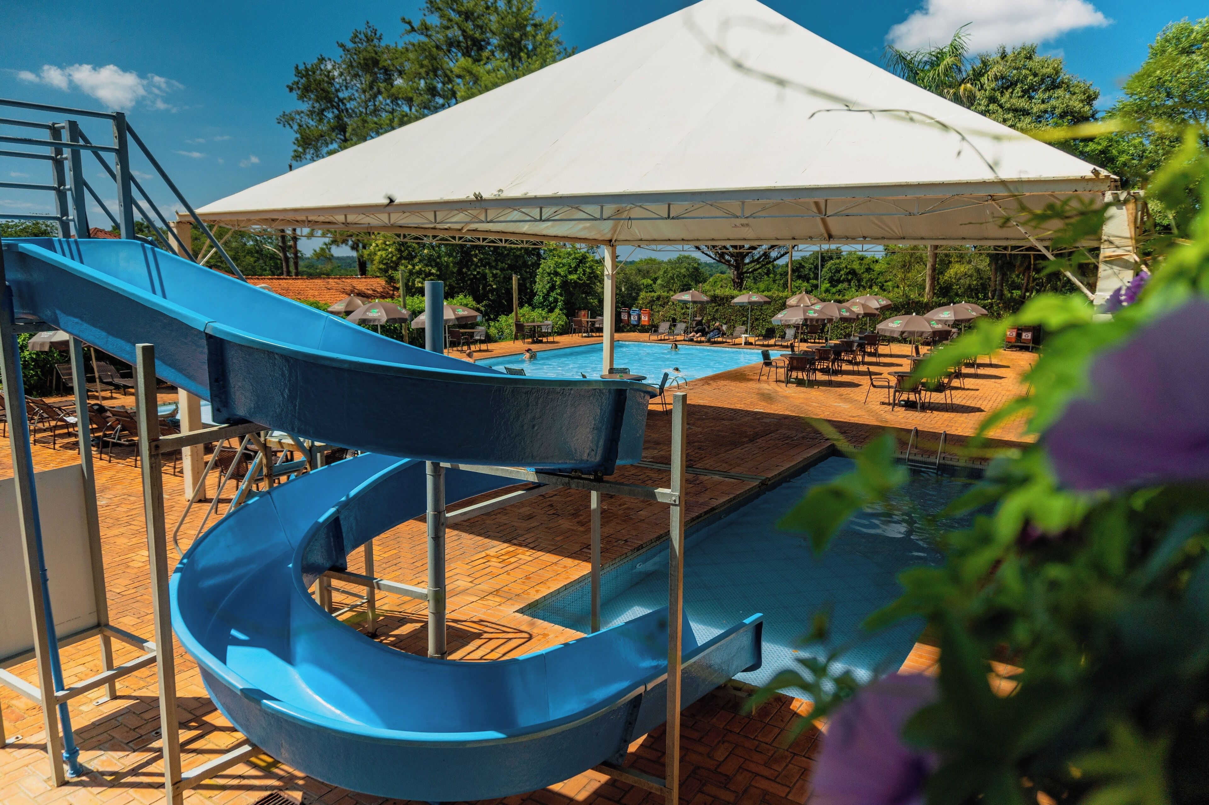 A pool area with a blue slide, umbrellas, and lounge chairs.