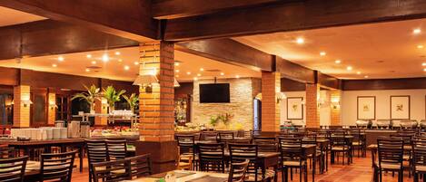 A spacious restaurant with high ceilings, brick walls, and numerous tables and chairs.