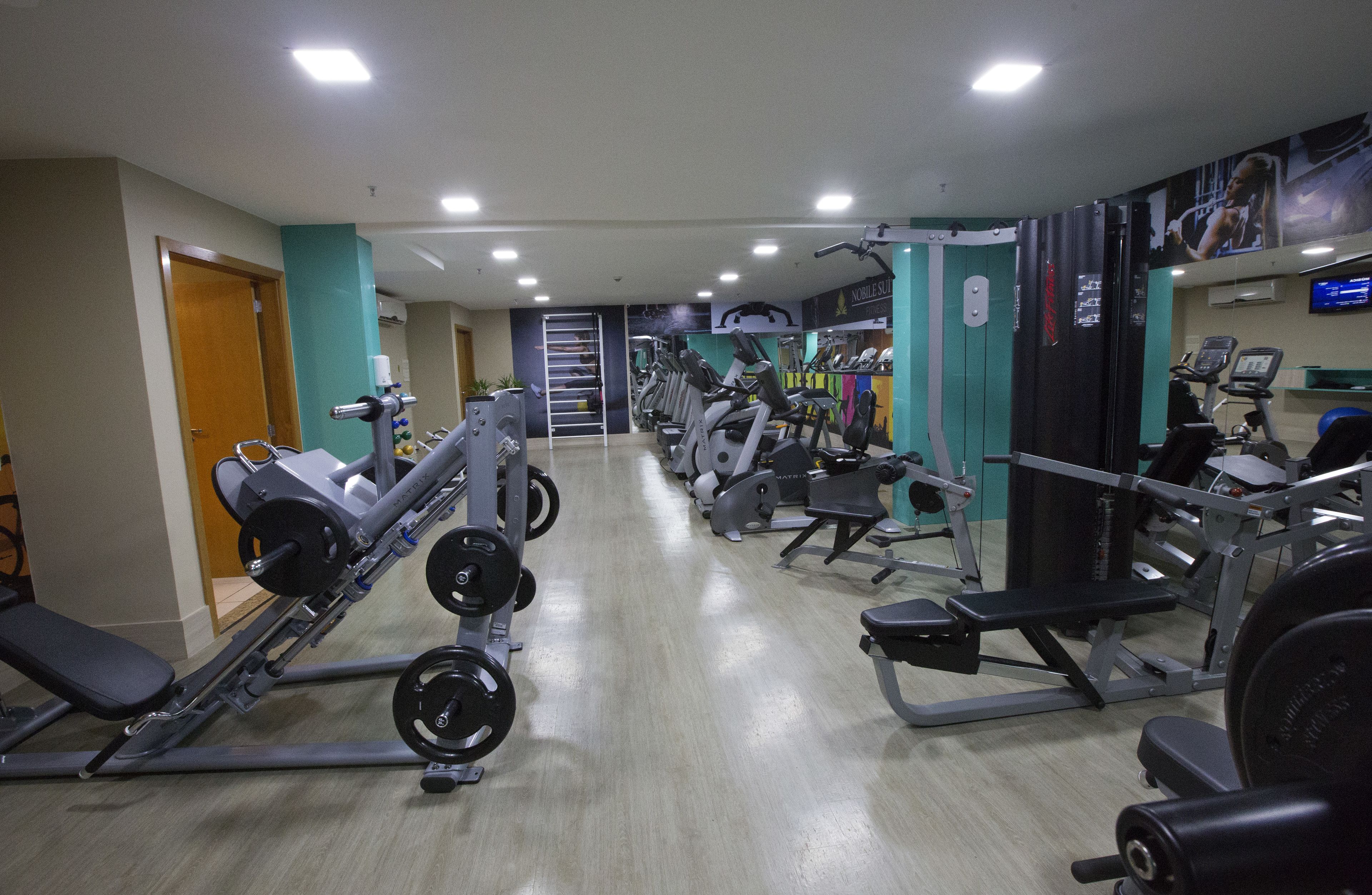 A gym with various exercise machines, a weight bench, and a wall-mounted TV.