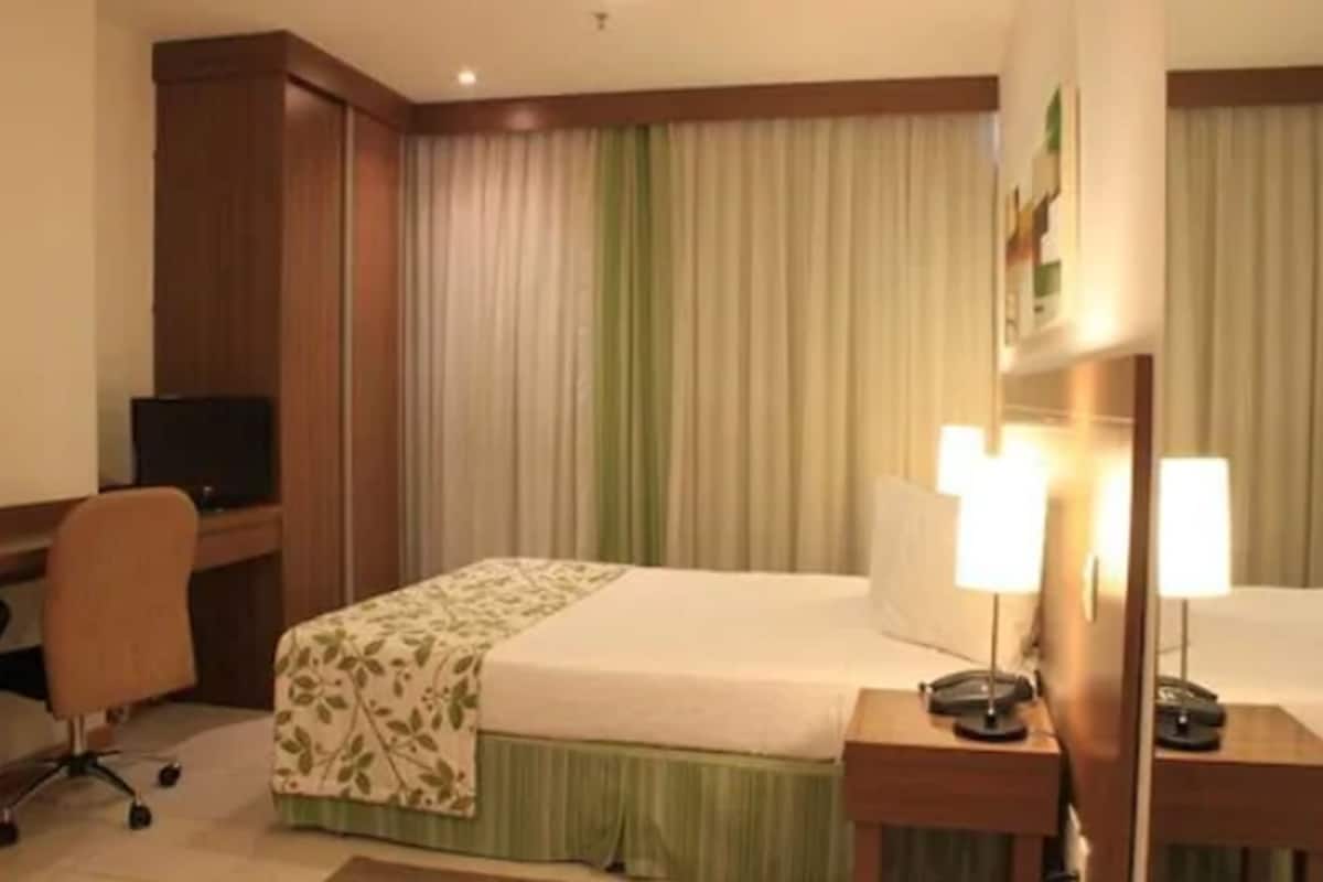 Una habitación de hotel con una cama, un escritorio con computadora, una silla y un televisor.