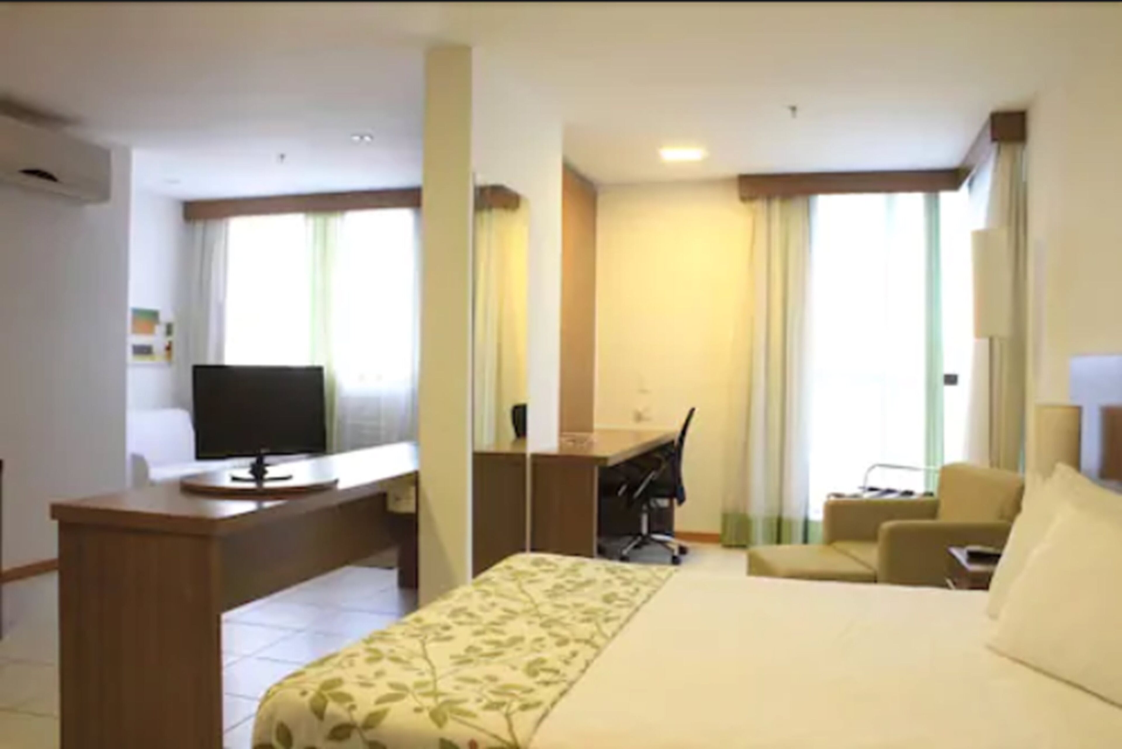 Une chambre d’hôtel équipée d’un lit, d’un bureau, d’une chaise, d’une télévision et d’une fenêtre avec des rideaux.
