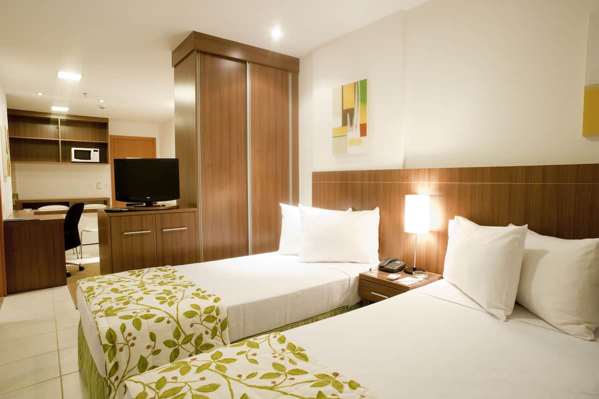 Habitación de hotel con dos camas, un escritorio con computadora, televisor y microondas.