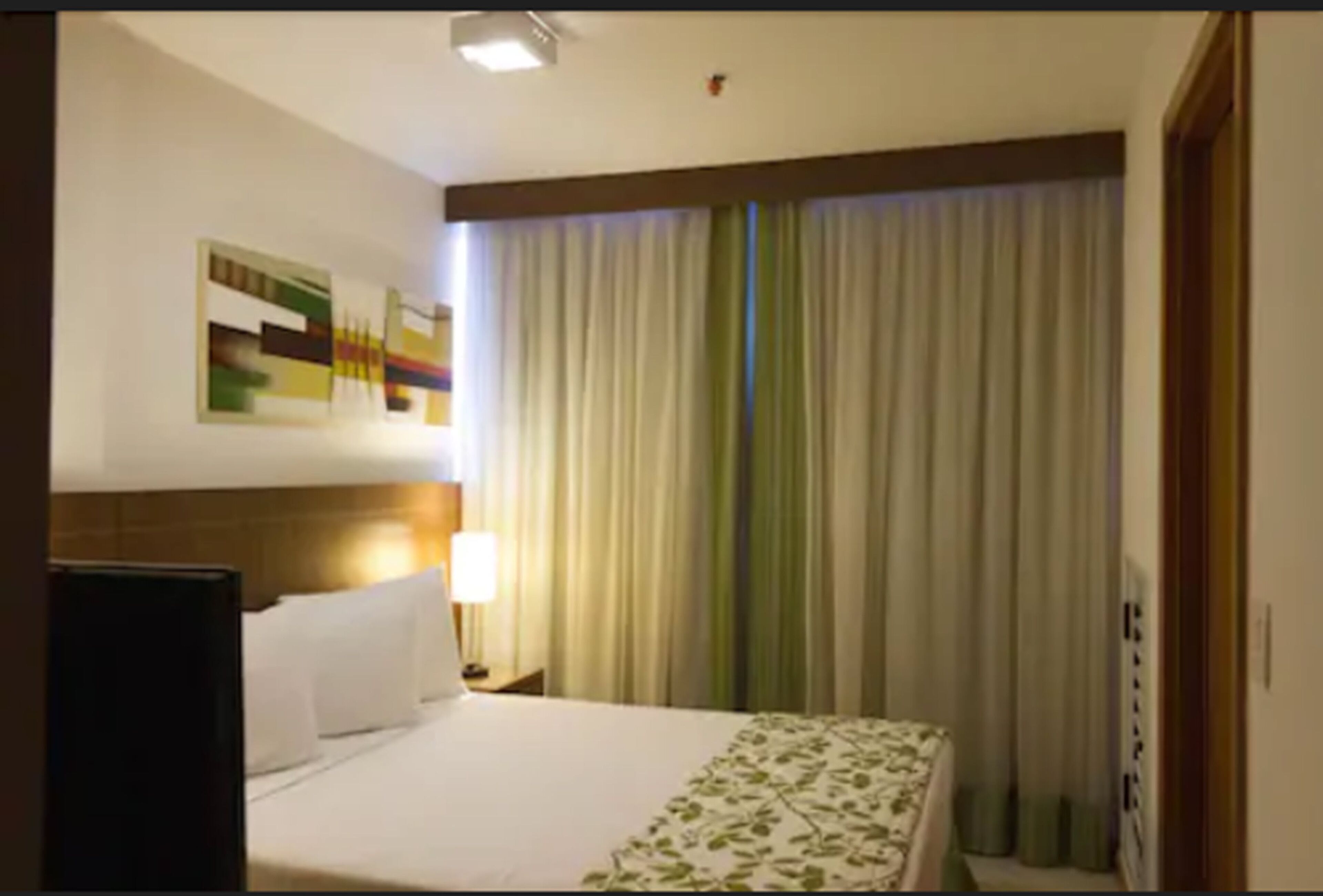 Una habitación de hotel con cama, mesita de noche, lámpara y un cuadro en la pared.