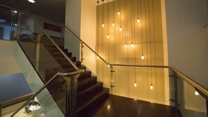 A modern staircase with glass railings and wooden steps, illuminated by hanging light bulbs. - Nobile Suites Monumental (Brasília)