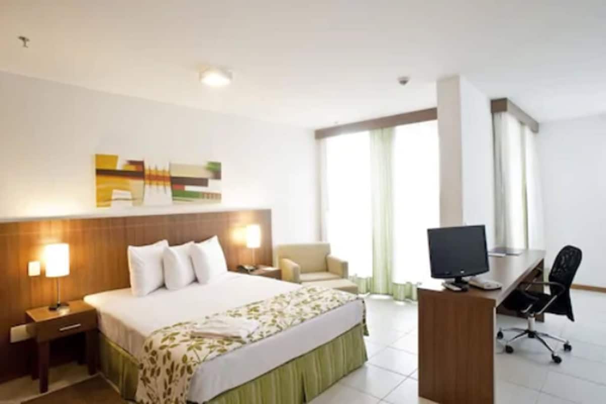 Habitación de hotel con cama, escritorio, computadora, silla y televisor.