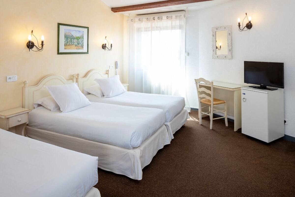 A hotel room with two beds, a desk with a television, and a chair.
