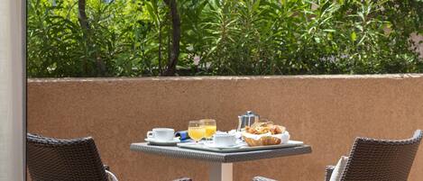 A table set with breakfast items, two wicker chairs, and a view of lush greenery.