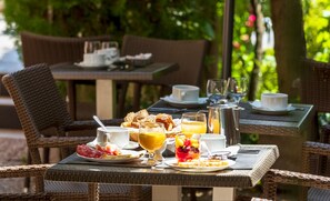 An outdoor dining area with wicker furniture, breakfast items, and a coffee pot. - Hôtel Le Mozart (Aix-en-Provence)