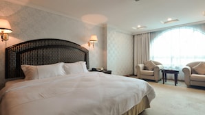 A hotel room with a large bed, two armchairs, a small table, and a large window with curtains. - New Pearl River (Guangzhou)