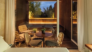 Un interior moderno con una mesa redonda, sillas de mimbre y vistas a árboles a través de una puerta de cristal.