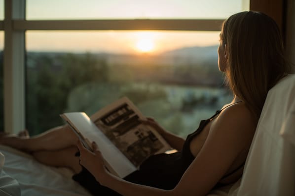 Una persona leyendo un libro junto a una ventana con vistas a la puesta de sol.