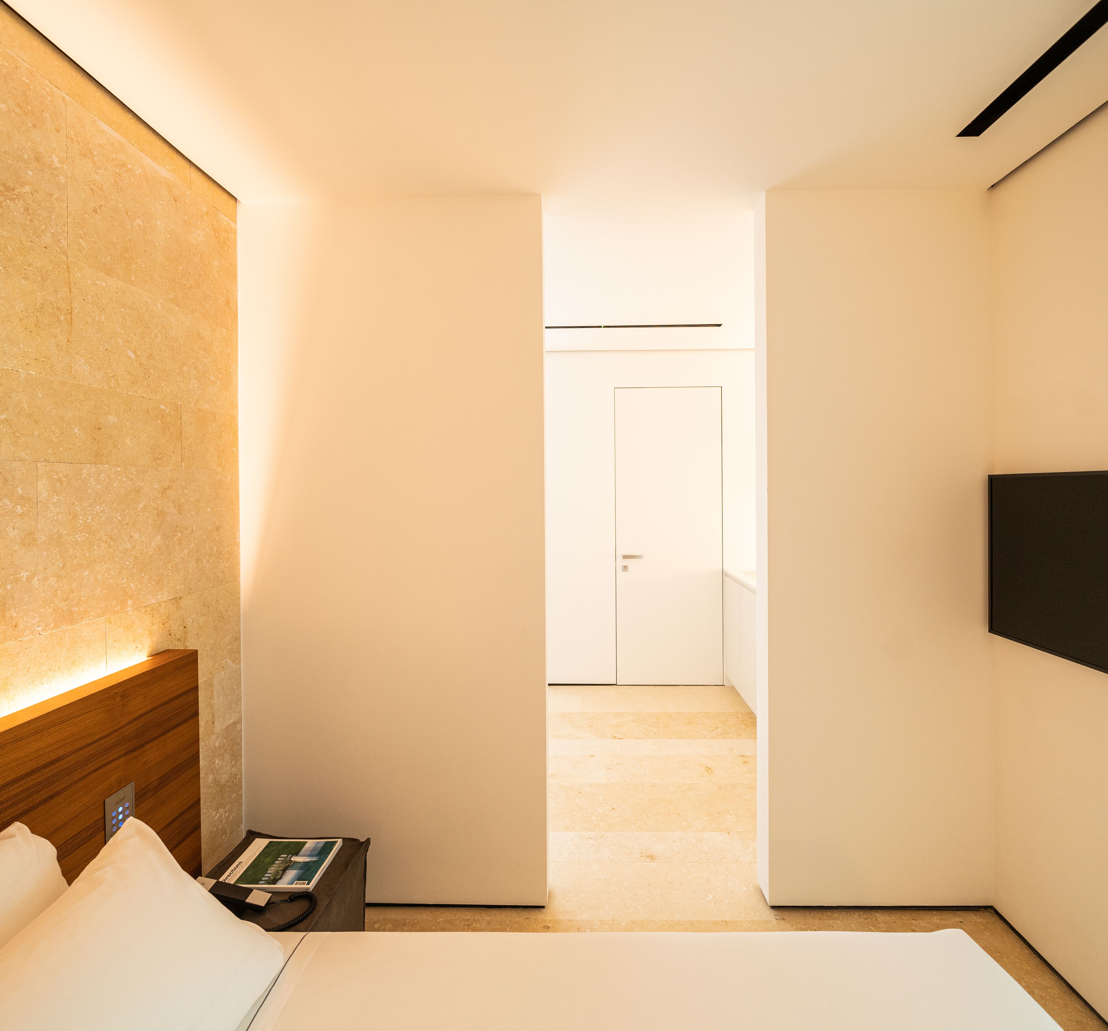 A hotel room with a bed, bedside table, and a TV mounted on the wall.