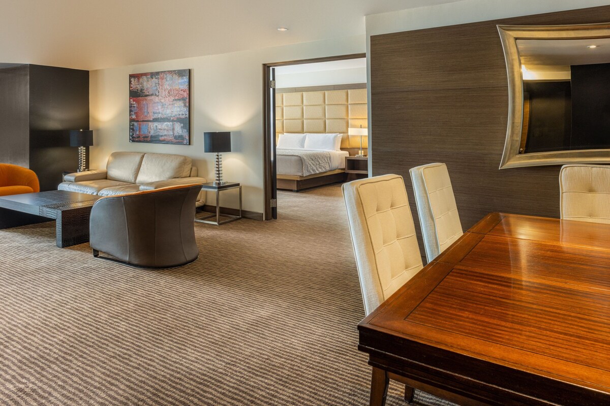 A modern hotel room with a dining area, a sofa, a bed, and a large mirror.