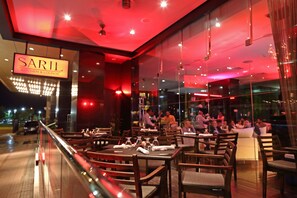 A restaurant with tables set for dining, a visible sign reading "SARIL KITCHEN & LOUNGE," and a view of the street outside.