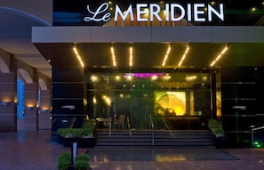The exterior of Le Meridien hotel with illuminated signage, a modern entrance, and a well-lit facade.